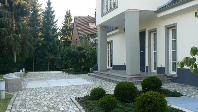 Eingangsbereich mit großen Sichtbetonplatten und Muschelkallpflaster.